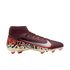 A profile view of a maroon Nike Mercurial soccer cleat against a black background. The shoe features a sock-like ankle collar, silver Swoosh with a red outline, and a cream-colored soleplate with orange studs. A bold graphic pattern in black, orange, and