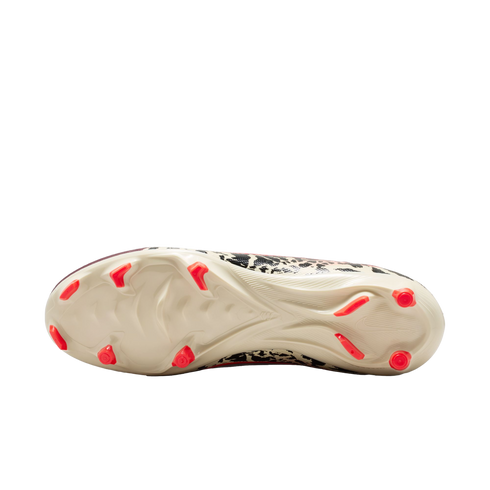 A bottom-up view of a cream-colored soccer cleat with bright orange studs and a black-and-white patterned upper against a solid black background.