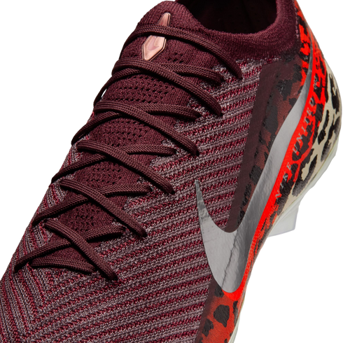 A close-up, angled view of a burgundy knit Nike soccer cleat with matching laces. It features a large metallic silver Nike swoosh on the side and a vibrant orange and black leopard print pattern on the heel.