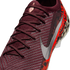 A close-up, angled view of a burgundy knit Nike soccer cleat with matching laces. It features a large metallic silver Nike swoosh on the side and a vibrant orange and black leopard print pattern on the heel.