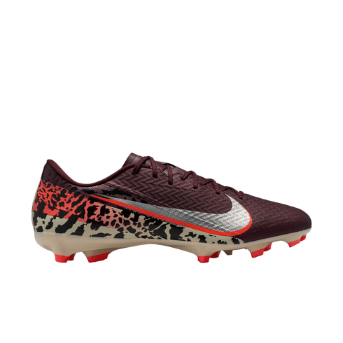 A profile view of a Nike soccer cleat against a solid black background. The shoe features a textured maroon upper, a large silver Nike Swoosh with an orange border, and a bold abstract graphic pattern in tan, black, and orange across the lower half and he