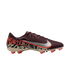 A profile view of a Nike soccer cleat against a solid black background. The shoe features a textured maroon upper, a large silver Nike Swoosh with an orange border, and a bold abstract graphic pattern in tan, black, and orange across the lower half and he
