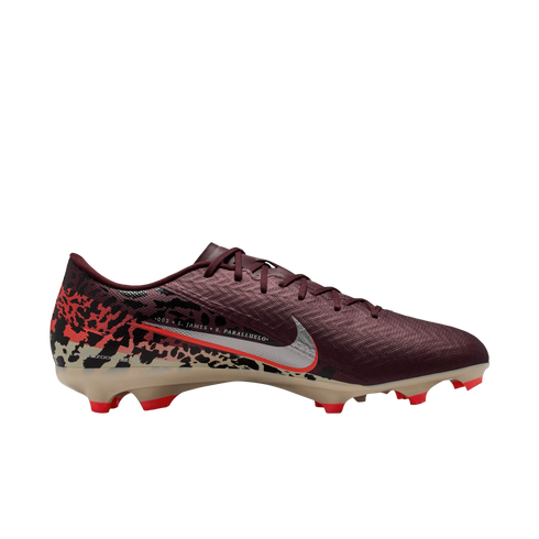 A side profile of a Nike soccer cleat against a solid black background. The shoe features a dark maroon textured upper, a silver Nike swoosh with a red outline, and a tan soleplate with bright red studs. A graphic pattern in red, black, and tan covers the