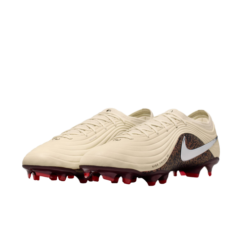 A pair of cream-colored Nike soccer cleats with a textured upper, animal-print heel, silver swoosh logo, and dark red studs against a black background.