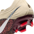 A close-up view of the heel and soleplate of a Nike soccer cleat against a black background. The upper features a cream-colored textured heel with a script "Maestro" inscription and a silver metallic Nike Swoosh. A glossy, deep-red translucent heel counte