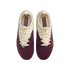 A top-down view of a pair of Nike football boots against a black background. The shoes feature a maroon lower section with horizontal ridges and a cream upper section. A black-and-white patterned trim lines the lace area, and small orange Nike swooshes ar