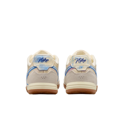 A rear view of a pair of Nike sneakers featuring cream and light gray suede uppers, script Nike logos on distressed blue heel tabs, and gum rubber outsoles against a solid black background.