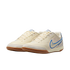 A pair of cream-colored Nike Tiempo indoor soccer shoes with blue accents and gum rubber soles, set against a black background.
