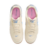 Top-down view of a pair of off-white Nike Tiempo Gato sneakers with light blue accents, pink insoles, and gum rubber outsoles, set against a solid black background.