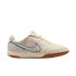 A profile view of a cream-colored Nike Tiempo indoor soccer shoe against a solid black background. The shoe features a blue-outlined Nike swoosh with a faded purple and blue interior, light grey suede overlays on the toe and heel, and a brown gum rubber o