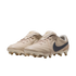 A pair of cream-colored Nike soccer cleats with a dark grey swoosh and gold accents, shown against a solid black background.