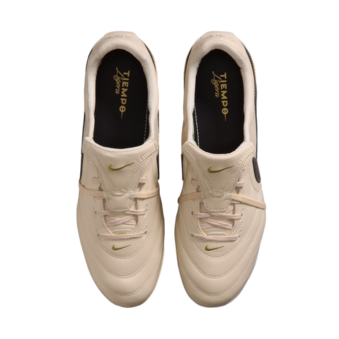 A top-down view of a pair of cream-colored Nike Tiempo Ligera soccer shoes with gold accents against a black background.