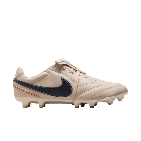 A side profile view of a tan leather Nike soccer cleat against a solid black background, featuring a dark navy blue swoosh and colorful stitching near the heel.