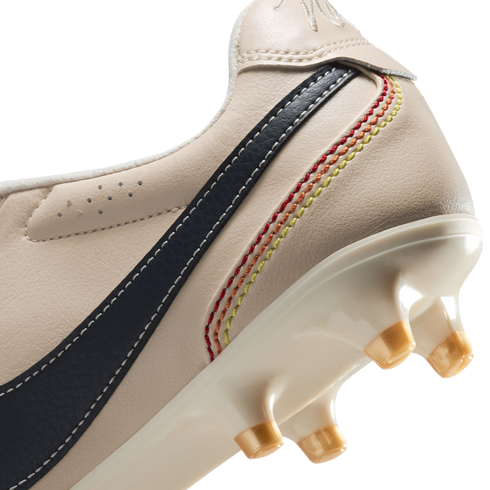 A close-up view of the heel and sole of an off-white leather soccer cleat. The shoe features a dark blue stripe with white stitching and five decorative, curved rows of stitching in a red, orange, and yellow gradient. The glossy white sole plate has trans