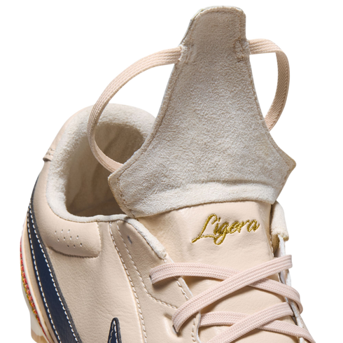 A close-up of a beige leather athletic shoe with its tongue flipped up. The word "Ligera" is embroidered in gold script above beige laces.