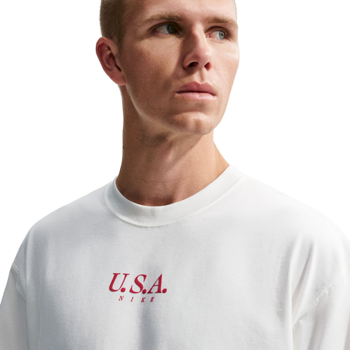A man in a white Nike crewneck t-shirt with red "U.S.A. NIKE" text on the chest, looking off to the side against a solid black background.