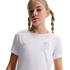Young girl with blonde pigtail braids wearing a white Nike athletic shirt with a shield crest, posed against a solid black background.