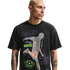 A man with a shaved head and mustache wears a black graphic t-shirt against a solid black background. The shirt features a large grey and peach-colored silhouette of an athlete in motion, surrounded by various purple and green sports-themed logos and text