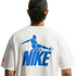 A back view of a person with dark, curly hair tied in a bun, wearing a white t-shirt against a black background. The shirt features a large blue graphic on the back consisting of a stylized soccer player kicking a ball, positioned above the word "NIKE" in