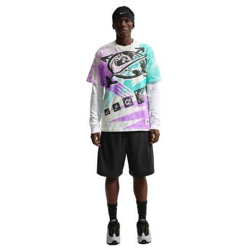 A person modeling a colorful purple, teal, and white graphic Nike t-shirt layered over a white long-sleeve shirt, paired with black athletic shorts, a black beanie, and grey sneakers against a solid black background.