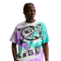 A young Black man with braided hair poses against a solid black background, wearing a white Nike t-shirt with a large, vibrant graphic. The shirt's central design features a black globe with a Nike swoosh wrapped around it, surrounded by bold, textured sp