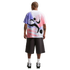 A rear view of a man standing against a black background. He is wearing a white oversized t-shirt with a large pink, purple, and black abstract graphic on the back, dark gray knee-length shorts, white crew socks, and black and white athletic shoes.