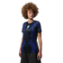 A person with a large curly afro wearing a blue and black patterned Brazil national team jersey, looking to the side against a black background.