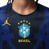 Close-up of a navy blue Brazil soccer jersey featuring a yellow Jumpman logo and the CBF crest with five stars above it, set against a background of textured blue vertical lines.
