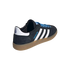 Adidas Handball Spezial sneaker in black suede with white stripes, blue laces, and gum sole, shown from a rear three-quarter angle on a solid black background.