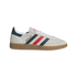 A side profile of an Adidas Handball Spezial sneaker featuring an off-white suede upper, green and red stripes, and a gum rubber sole against a black background.