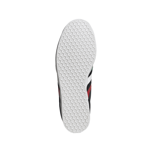 Top-down view of a white sneaker sole with a hexagonal grip pattern. Parts of the black upper with red and white stripes are visible against a solid black background.