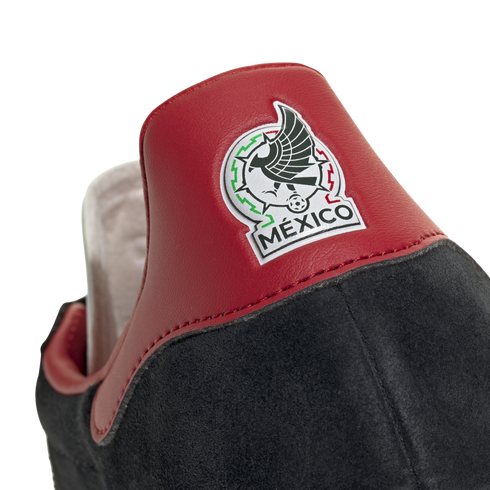 Close-up of the heel of a black suede shoe with a red leather tab featuring the embroidered Mexico national football team logo.