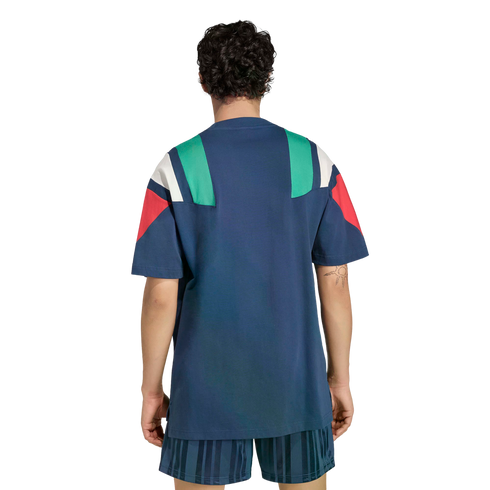 Rear view of a person wearing a navy blue t-shirt with green, white, and red geometric panels on the shoulders and matching blue striped shorts.