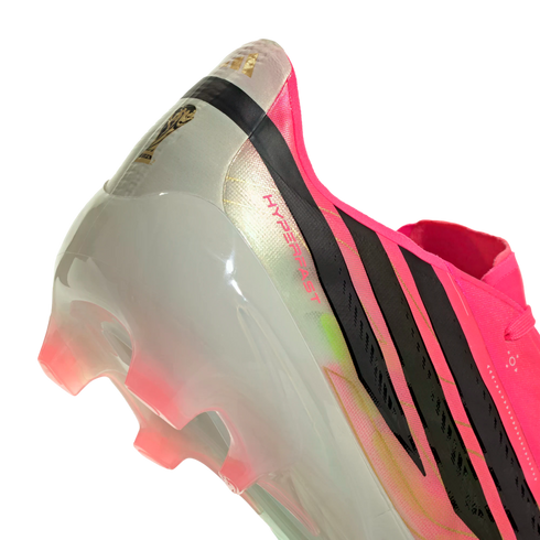 Close-up of the heel of a pink and white Adidas soccer cleat with black stripes, a gold FIFA logo, and translucent pink studs.