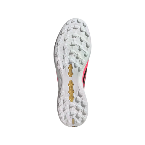 Underside of a white Adidas Predator soccer shoe showing a multi-studded turf outsole with gold plates and pink accents.