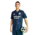 A man in a navy Olympique Lyonnais soccer kit with red and blue stripes, holding a soccer ball against a black background.
