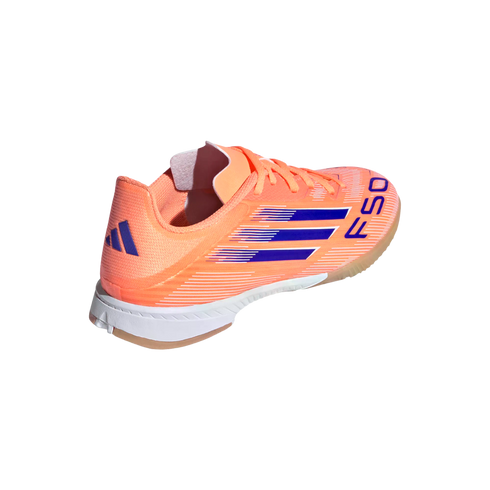 A peach-colored Adidas F50 indoor soccer shoe with navy blue stripes and logo against a black background.