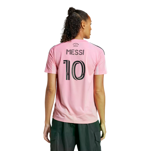 Rear view of a person wearing a pink Inter Miami soccer jersey with "MESSI 10" on the back and dark cargo pants against a white background.