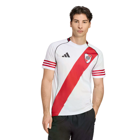 A man wearing a white River Plate football jersey with a red diagonal sash and black shorts against a plain white background.