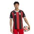 A man in a red and black striped River Plate soccer jersey and red shorts holds a soccer ball against a white background.