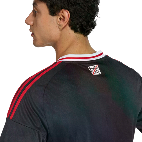 Profile and back view of a man wearing a black sports jersey with red stripes on the shoulders and a small "River Plate" logo on the upper back.