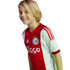 A smiling blonde child wearing a red and white Ajax football jersey.
