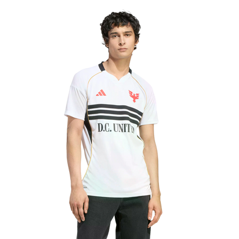 A man with dark curly hair wearing a white D.C. United soccer jersey with three black horizontal stripes across the chest, posing against a solid black background.