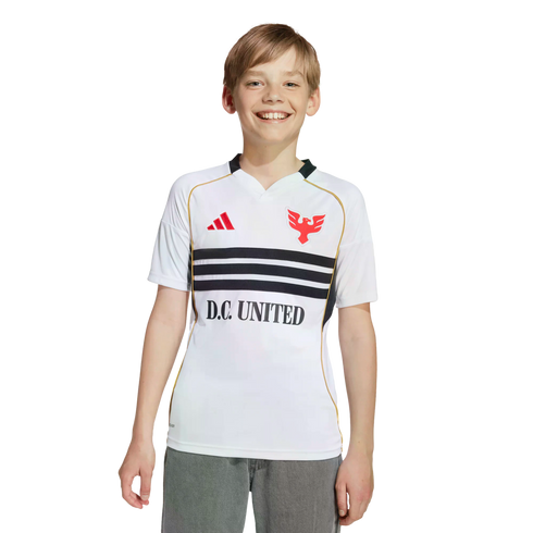 A smiling young boy in a white D.C. United soccer jersey and grey pants against a black background.