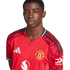 Studio portrait of a young Black man wearing a red Manchester United football jersey against a white background.
