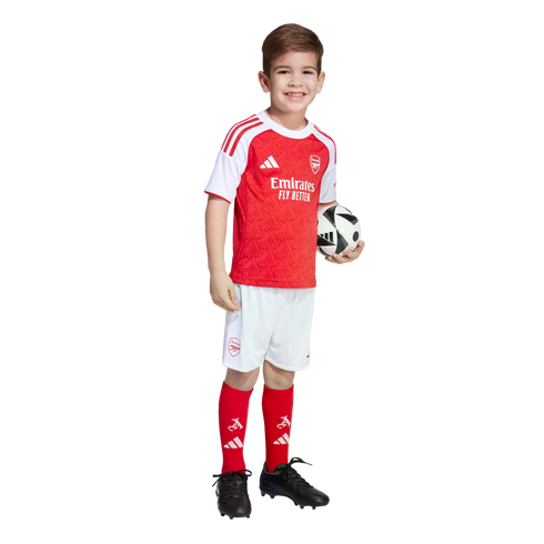 A smiling boy in an Arsenal football kit holds a soccer ball against a white background.