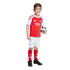 A smiling boy in an Arsenal football kit holds a soccer ball against a white background.