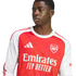 Close-up of a young man wearing a red and white Arsenal jersey with an Adidas logo and "Emirates FLY BETTER" text, looking sideways against a white background.