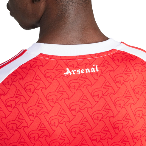 A close-up of the back of a red Arsenal jersey with a white collar, featuring a repeating "A" pattern and "Arsenal" printed in white gothic font below the neckline.