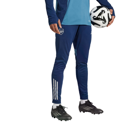 Person in blue Arsenal FC training gear and black soccer cleats holding a soccer ball against a black background.